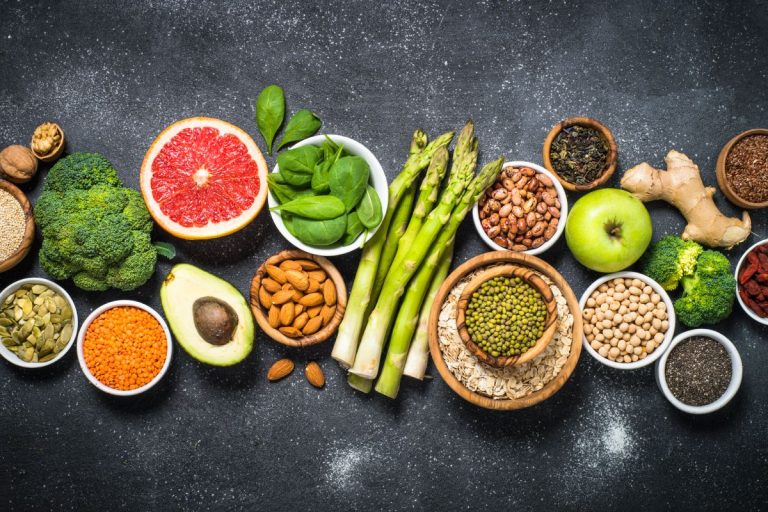 Superfoods on black stone background. Organic food and healthy vegan food. Legumes, nuts, seeds, fruit and vegetables. Top view.